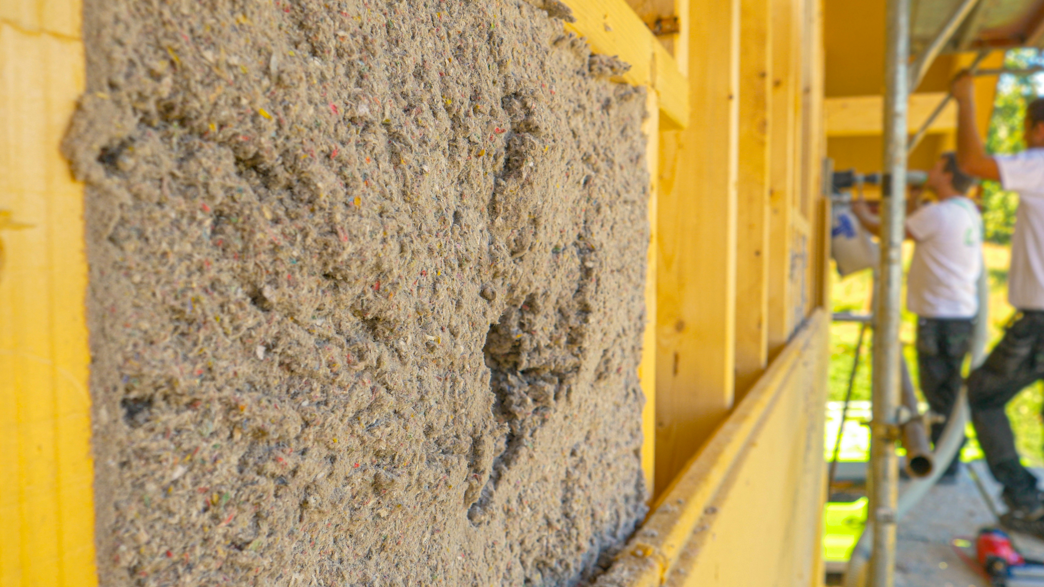 Workers installing cellulose insulation on the side of a building